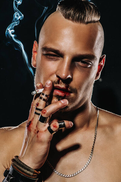 Портрет жестокого красавца с обнаженным туловищем, курящего сигарету. Мужская красота, здоровье. Рокер, панк
. 