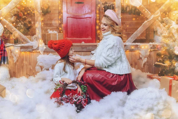 Happy mom and daughter are posing near the house, decorated for Christmas. Seasonal winter fashion. Merry Christmas and Happy New Year.