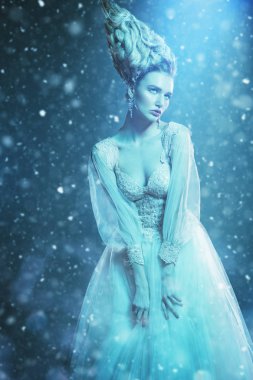 Kabarık elbise ve stüdyoda mavi arka plan üzerinde poz soğuk bir güzel Bayan portresi. Güzellik, kozmetik, saç modeli, moda.