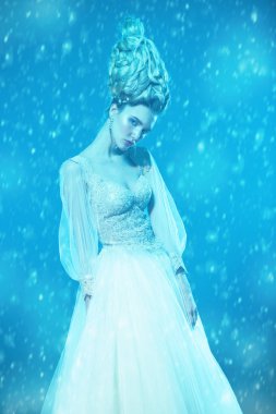 Kabarık elbise ve stüdyoda mavi arka plan üzerinde poz soğuk bir güzel Bayan portresi. Güzellik, kozmetik, saç modeli, moda.