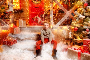 Şirin çocuk çocuk Noel için dekore edilmiş evinin yakınında oturan ve kar ile oynuyor. Mucizeler zamanı. Mutlu Noeller ve mutlu yeni yıl.