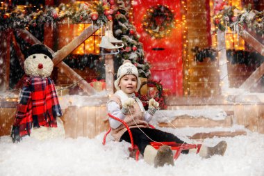 Kış giysileri ve bir şapka hoş küçük çocuk Noel Baba'nın sihirli ev kızak önünde oturuyor. Mucize zamanı. Mutlu Noeller ve mutlu yeni yıl.
