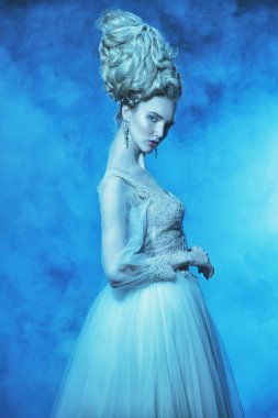 Kabarık elbise ve stüdyoda mavi arka plan üzerinde poz soğuk bir güzel Bayan portresi. Güzellik, kozmetik, saç modeli, moda.