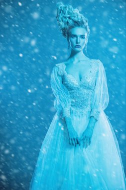 Kabarık elbise ve stüdyoda mavi arka plan üzerinde poz soğuk bir güzel Bayan portresi. Güzellik, kozmetik, saç modeli, moda.