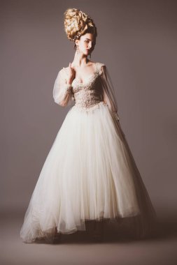 Kabarık elbise ve stüdyoda gri arka plan üzerinde poz soğuk bir güzel bayan bir tam uzunlukta portresi. Güzellik, kozmetik, saç modeli, moda.