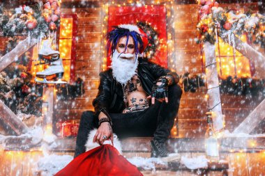 Cool punk Santa fools around near his house with a bag of gifts in his hands. clipart