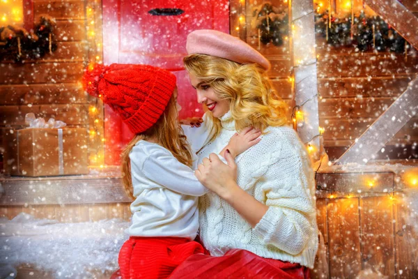 Happy mom and daughter are posing near the house, decorated for Christmas. Seasonal winter fashion. Merry Christmas and Happy New Year.