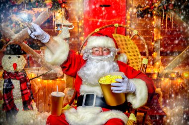 Noel Baba portresi sallanan sandalyede oturan ve patlamış mısır ve uzaktan kumanda elinde tutuyor. Noel ve yeni yıl kavramı.