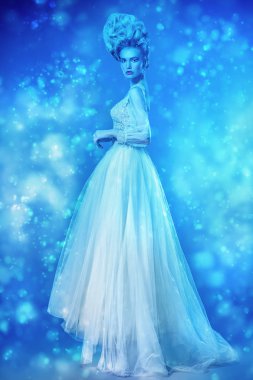 Kabarık elbise ve stüdyoda mavi arka plan üzerinde poz soğuk bir güzel bayan bir tam uzunlukta portresi. Güzellik, kozmetik, saç modeli, moda.