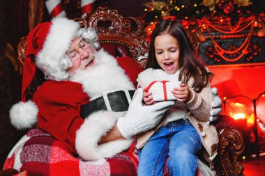 Mutlu bir genç kız Noel Baba yakınındaki bir hediye ile evde oturuyor. Mutlu Noeller ve mutlu yeni yıl.