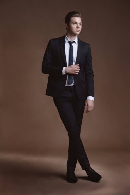 Şık takım elbise kahverengi arka plan üzerinde poz yakışıklı genç adam. İş tarzı. Erkek güzellik, moda. Saç modeli.