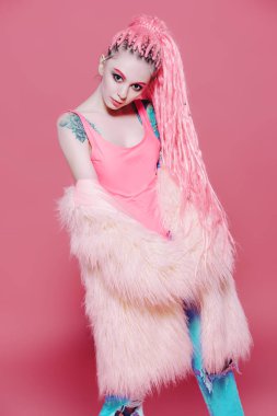 Şık kız pembe dreadlocks pembe bir arka plan üzerinde parlak giysiler içinde poz ile. Güzellik, moda.