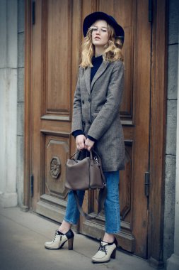 Bir palto ve şapka zarif genç kadın sokakta poz. İlkbahar ve sonbahar moda.