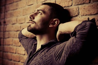 Yakın çekim portre yakışıklı bir brunet adamın üzerinde tuğla duvar arka plan. Erkek güzelliği, moda. Erkek Berber Dükkanı, saç modeli.