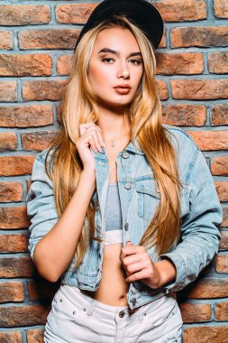 Uzun sarı saçlı kot giyen serin modern kız giysi ve beyzbol kap ayakta duvara tarafından. Hippi tarzı. Gençlik moda.