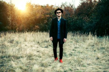 Sonbahar moda. Yakışıklı erkek model siyah ceket, şapka ve güneş gözlüğü açık poz. Sonbahar doğa.