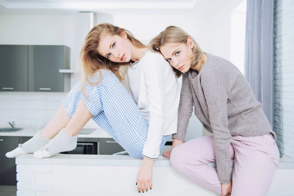 Two girlfriends are posing  in home clothes at the home.