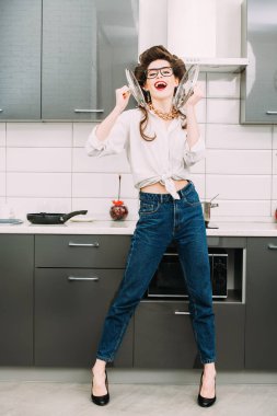 Güzel kız saçında curlers ile günlük giysiler içinde poz ve mutfak eşyaları ile oynuyor. Moda ev atış. Tam uzunlukta portre. 