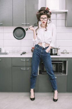 Güzel kız saçında curlers ile günlük giysiler içinde poz ve pan tutarak oynamaya. Moda ev atış. Tam uzunlukta portre. 