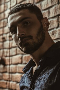 Yakın çekim portre yakışıklı bir brunet adamın üzerinde tuğla duvar arka plan. Erkek güzelliği, moda. Erkek Berber Dükkanı, saç modeli.