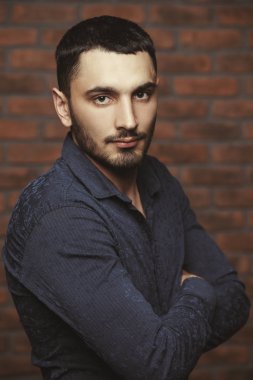 Yakışıklı bir brunet adam ayakta bir tuğla duvar tarafından portresi. Erkek güzelliği, moda. Erkek Berber Dükkanı, saç modeli.