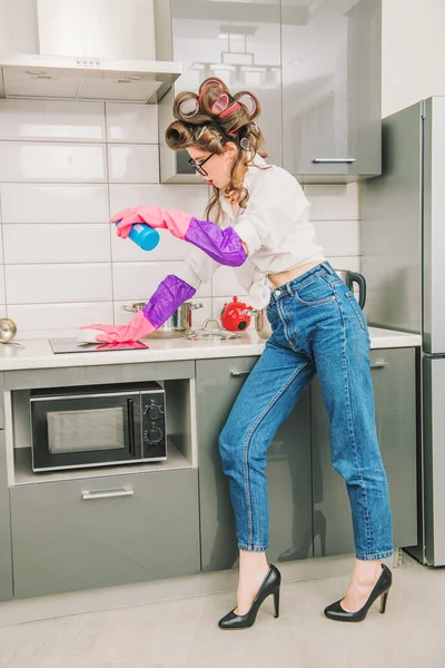 Attractive housewife in casual clothes is cleaning with detergent the countertop of the kitchen set. Fashion home shot. Full length portrait.