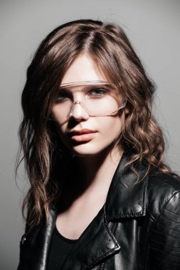 Deri ceket gri arka plan üzerine gözlük ile şık moda kadın modelinde portresi. Güzellik, moda kavramı. Stüdyo vurdu.
