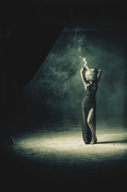 Güzel bir sarışın bayan kalıntıları arka planda bir sigara ile poz olduğunu. Gece elbisesi. Moda, güzellik.