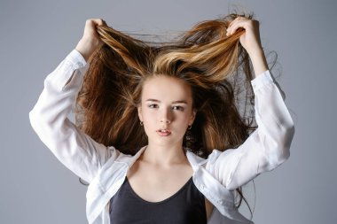 Teen tarzı. Güzel genç model uzun saçlı beyaz gömlekli stüdyoda poz. Güzellik, moda. 