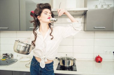 Güzel kız saçında curlers ile günlük giysiler içinde poz ve bir pot tutarak. Moda ev atış. Pin-up tarzı.