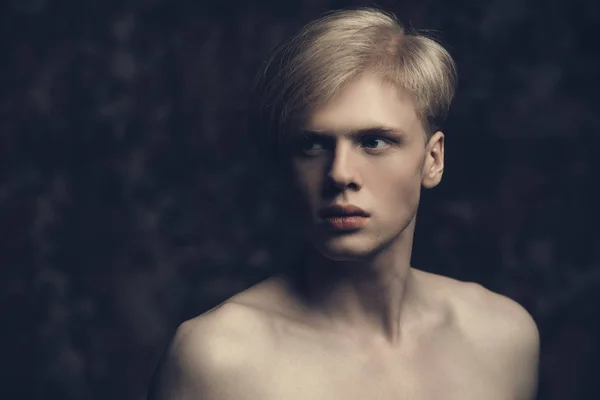 Portrait of a shirtless young man with blond hair posing at studio. Gray background. Men\'s health.