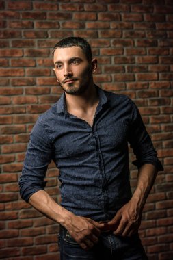 Yakışıklı bir brunet adam ayakta bir tuğla duvar tarafından portresi. Erkek güzelliği, moda. Erkek Berber Dükkanı, saç modeli.