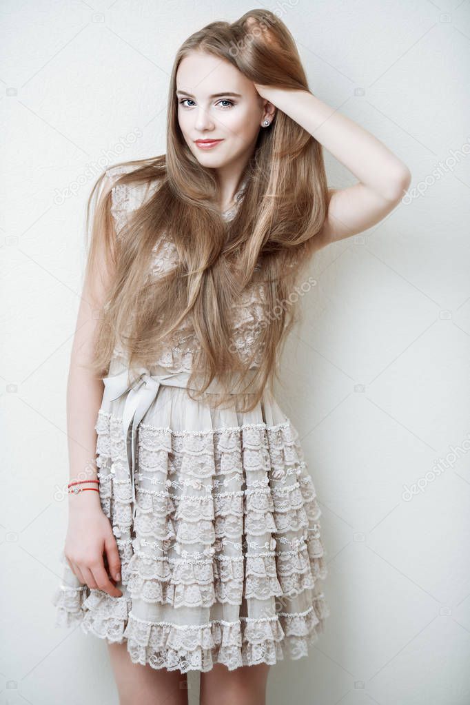 Portrait of a cute girl in standing lace dress and leaning on the wall in the room. Beauty, fashion.