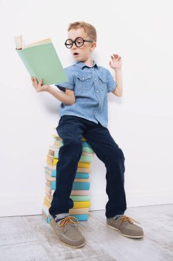 Kitaplar üzerinde oturan ve beyaz arka plan üzerinde poz Gözlüklü Şirin bir genç çocuk portresi. Güzellik, moda, okul, eğitim.