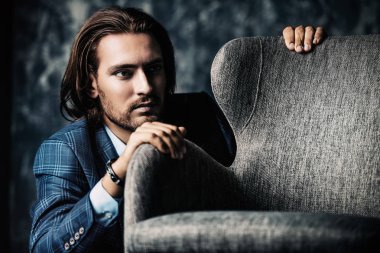 Vogue stüdyoda koltuk yakın oturan bir yakışıklı adam bir kadeh. Mobilya ve iç. Erkek güzellik, moda.