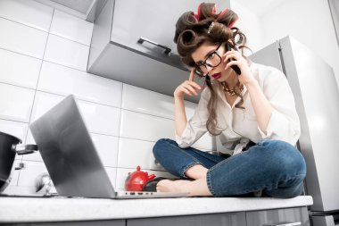 Güzel bir kız ile bir dizüstü bilgisayar ile saçında curlers günlük giysiler içinde poz portresi. Moda ev atış. Pin-up tarzı.