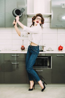 Günlük giysiler ve curlers çekici bir kız mutfakta bir tava ile ayarlamak anlamına gelir. Moda ev atış. Tam uzunlukta portre. 