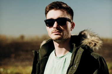 Bir ceket ve güneş gözlüğü takan yakışıklı acımasız bir adam. Moda erkekler için. Bahar, kış.