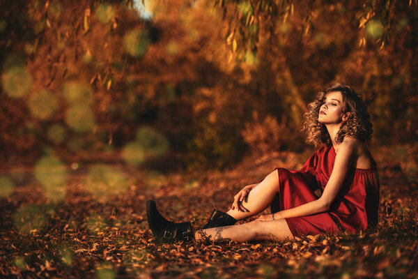 A beautiful young girl is posing in the countryside in a red dress. Fashion concept. Golden autumn.