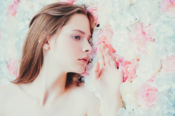 A close up portrait of a pretty young girl posing in the studio over the background with flowers. Beauty, cosmetics, skincare.