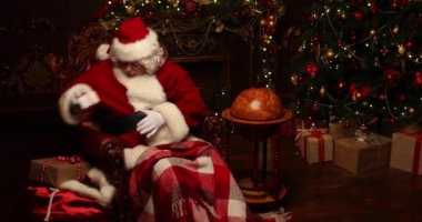 Noel Baba bir battaniye ile kaplı bir deri sandalyede oturuyor, Noel için dekore edilmiş bir odada hediye kutuları yakalamak. Noel ve Yeni Yıl zamanı.