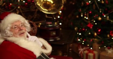 Dreamy Santa Claus Noel için dekore edilmiş bir odada deri bir sandalyede oturan gramofon müzik dinliyor. Noel ve Yeni Yıl zamanı. 