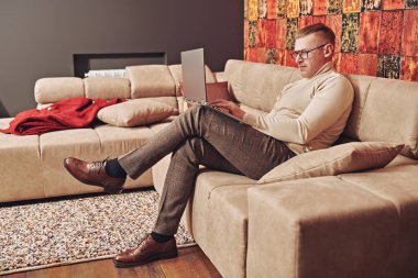 Zarif günlük kıyafetler ve gözlüklerle saygıdeğer orta yaşlı iş adamı evde dizüstü bilgisayarla çalışıyor. Başarılı yönetici kavramı.