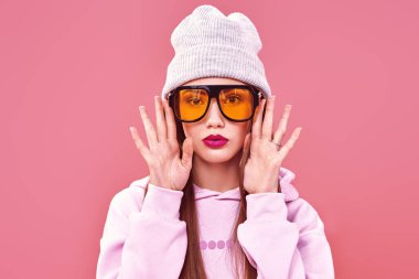 Pembe arka planda modern kıyafetler ve güneş gözlüğü takan parlak bir genç kız. Gençlik tarzı, moda. Stüdyo portresi. Boşluğu kopyala.