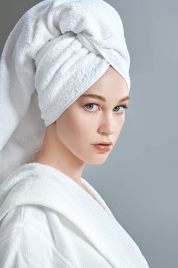 Beyaz bornozlu güzel bir genç kadın portresi ve duş aldıktan sonra saçının etrafına bir havlu. Güzellik, vücut bakımı, kaplıca.