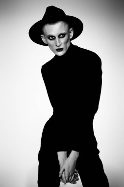 Siyah elbiseli ve açık renk şapkalı kadın makyajlı genç bir adamın portresi. Avangart.