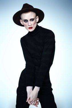 Siyah elbiseli ve açık renk şapkalı kadın makyajlı genç bir adamın portresi. Avangart.