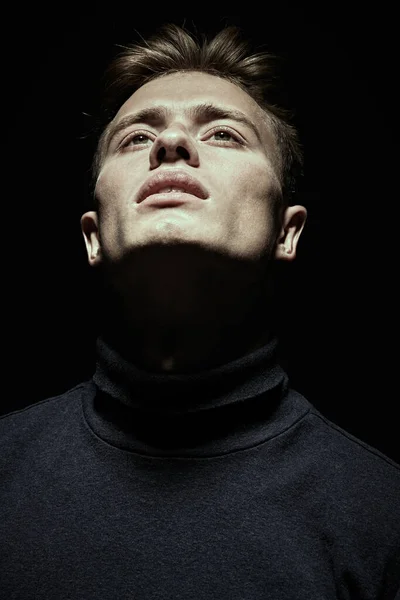 Portrait of a handsome young man in black clothes looking up on a black background.