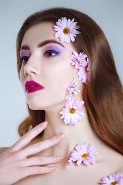 Güzel esmer bir kızın portresi. Yüzünde ve beyaz bir arka planda kasımpatı çiçekleri var. Güzellik, kaplıca ve kozmetik konsepti. 