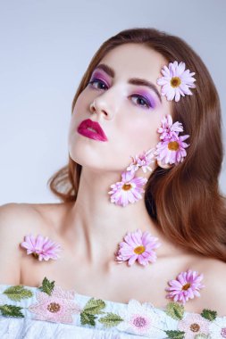 Güzel esmer bir kızın portresi. Yüzünde ve beyaz bir arka planda kasımpatı çiçekleri var. Güzellik, kaplıca ve kozmetik konsepti. 